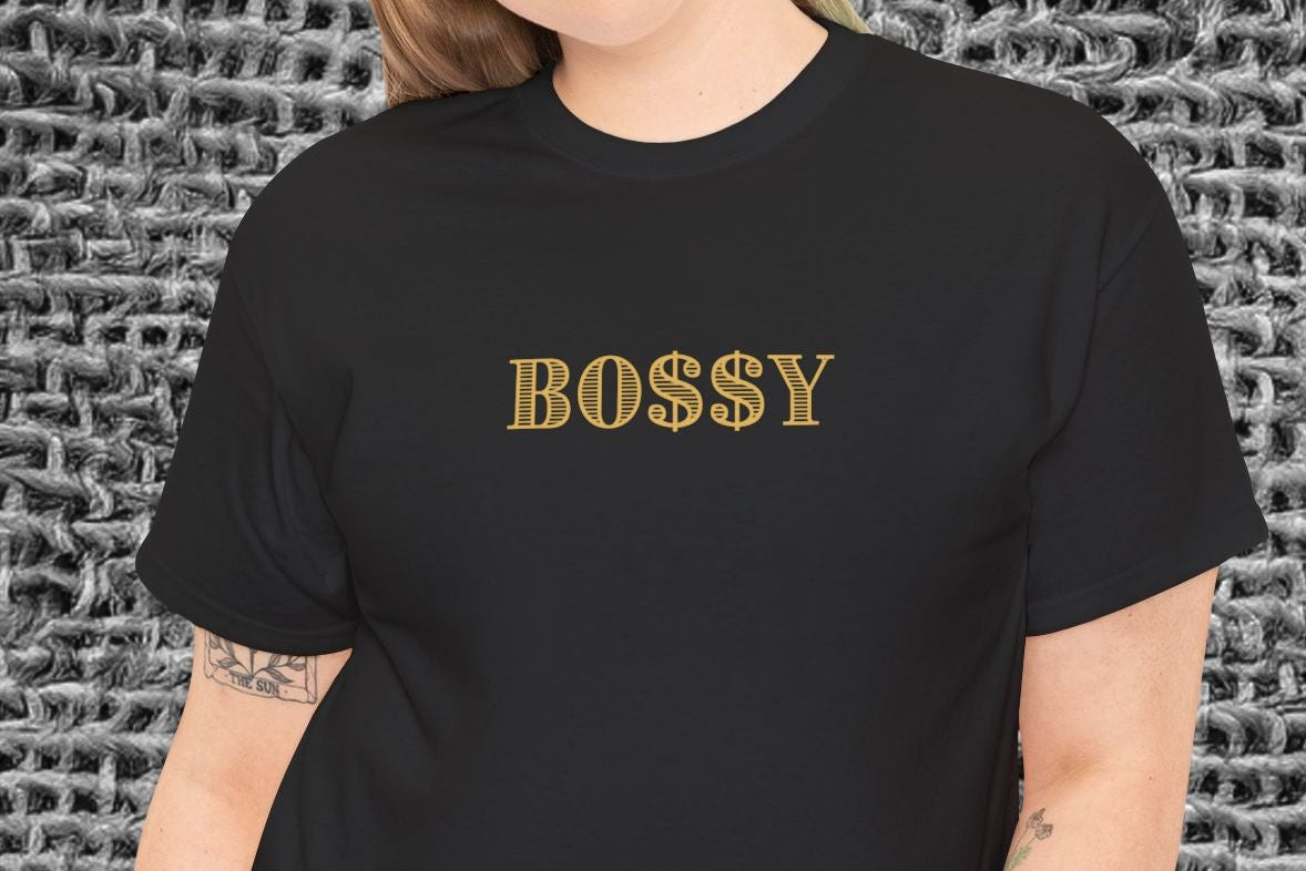 Person wearing a black t-shirt with 'BOSSY' text against a textured gray background