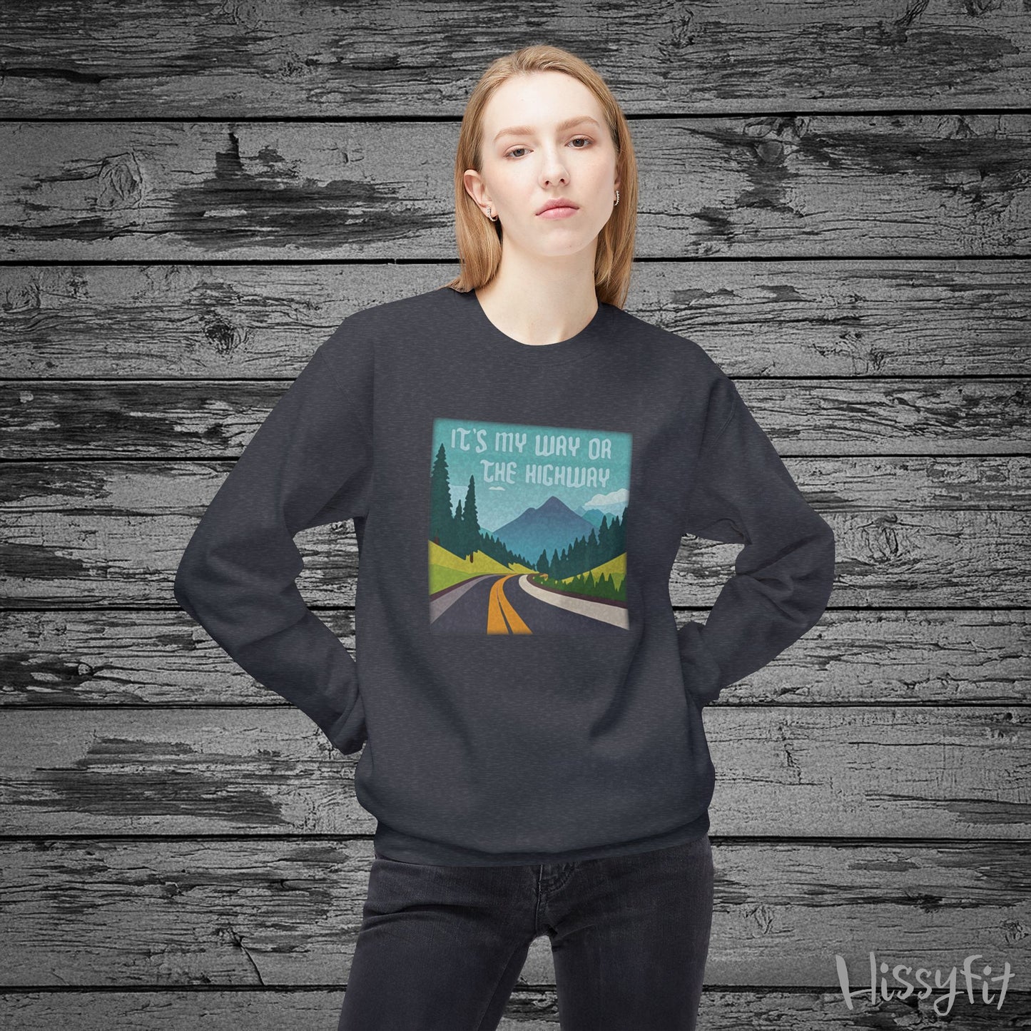 Person wearing a dark gray sweatshirt with a graphic design of a road and mountains and "It's my way or the highway" text on a wooden background