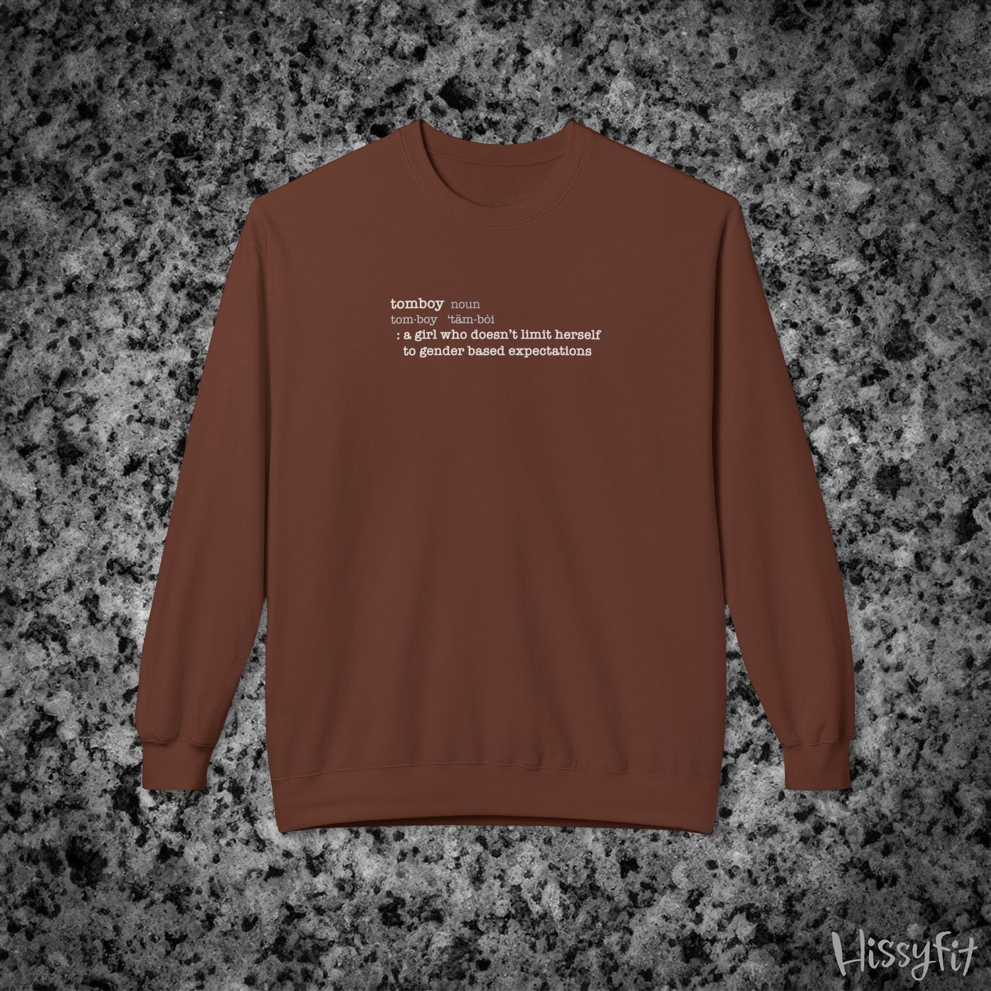 Brown sweatshirt with text definition of "Tomboy" on a gray and black speckled background