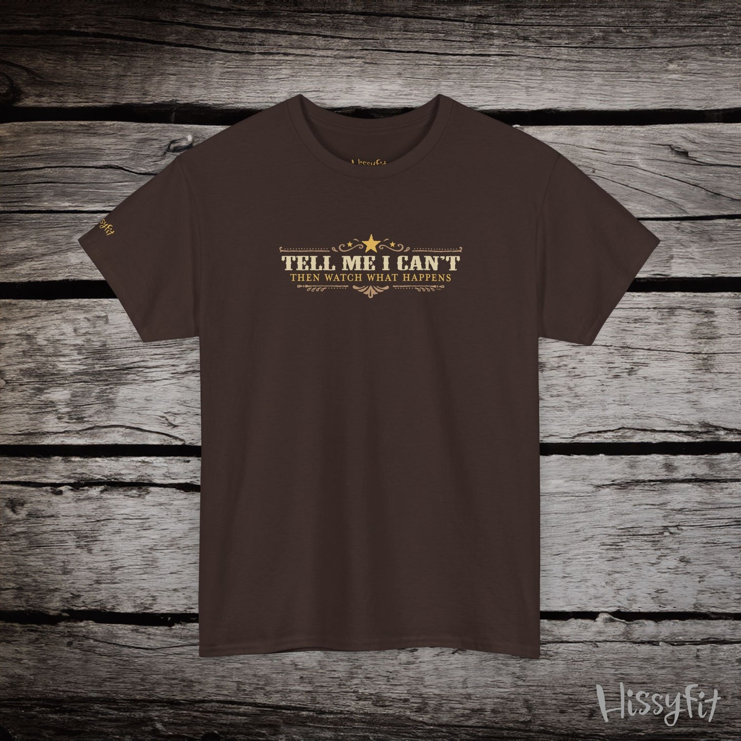 Brown t-shirt with text 'Tell me I can't then watch what happens' on a wooden surface, featuring the brand 'Hissyfit'.