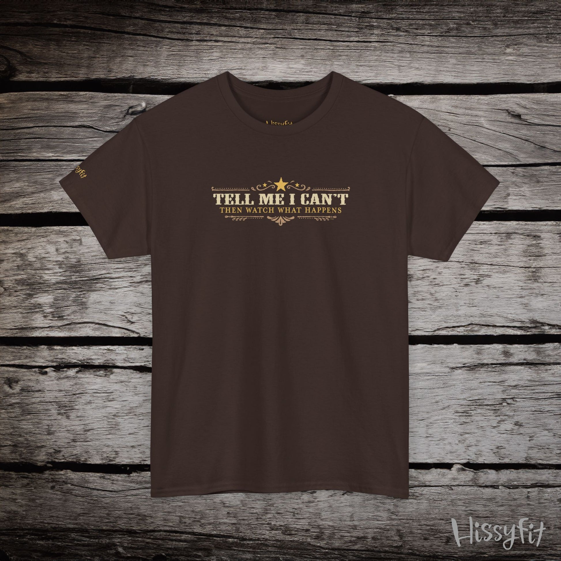 Brown t-shirt with text 'Tell me I can't then watch what happens' on a wooden surface, featuring the brand 'Hissyfit'.