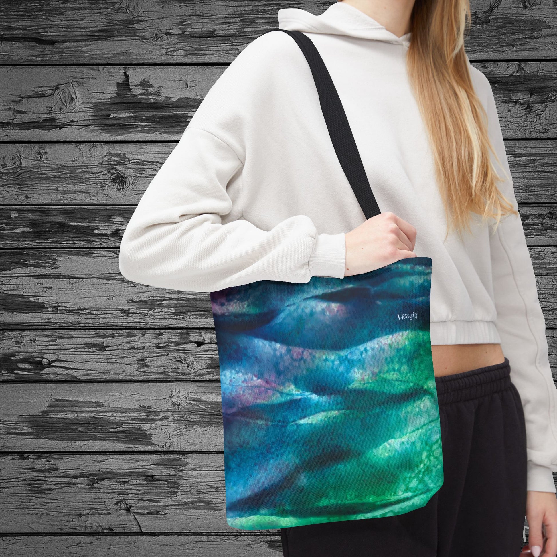 Person holding a tote bag with a colorful design against a wooden background