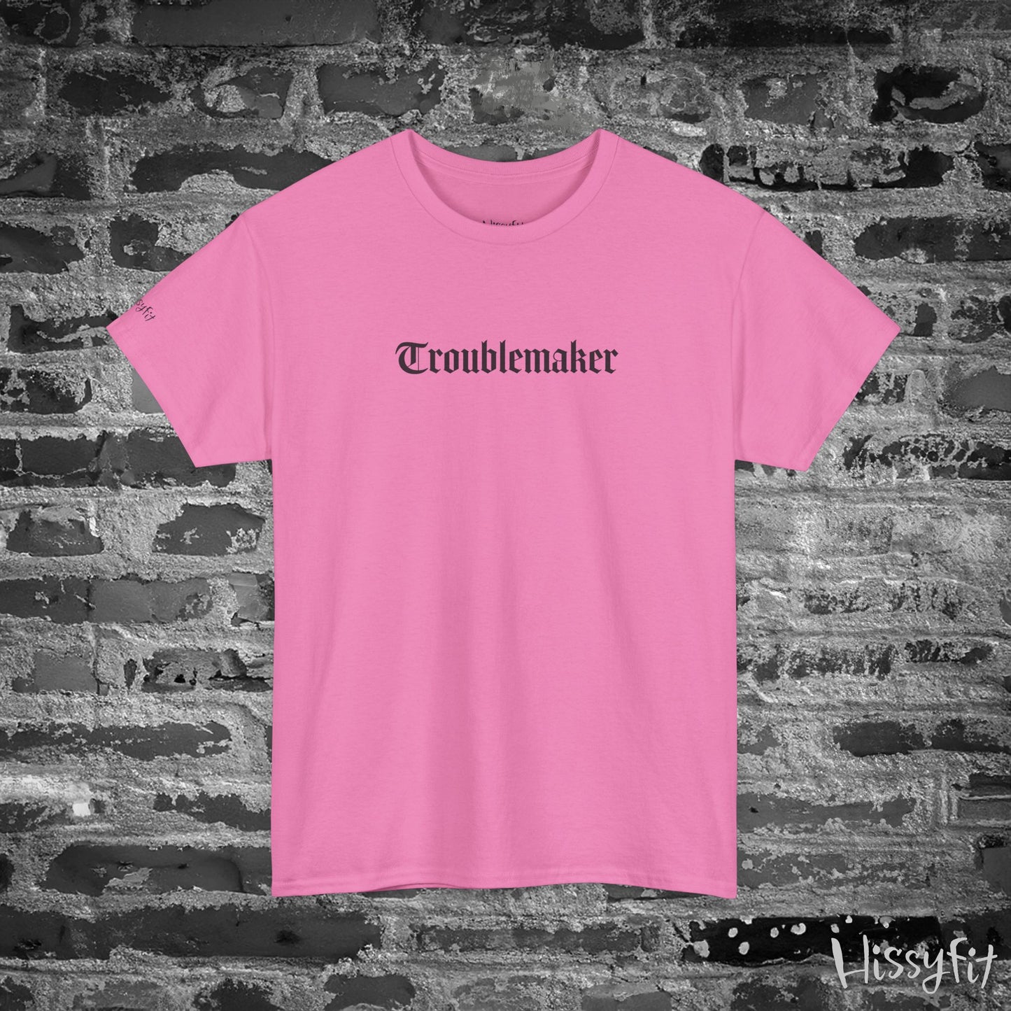 Pink t-shirt with 'Troublemaker' text on a brick wall background