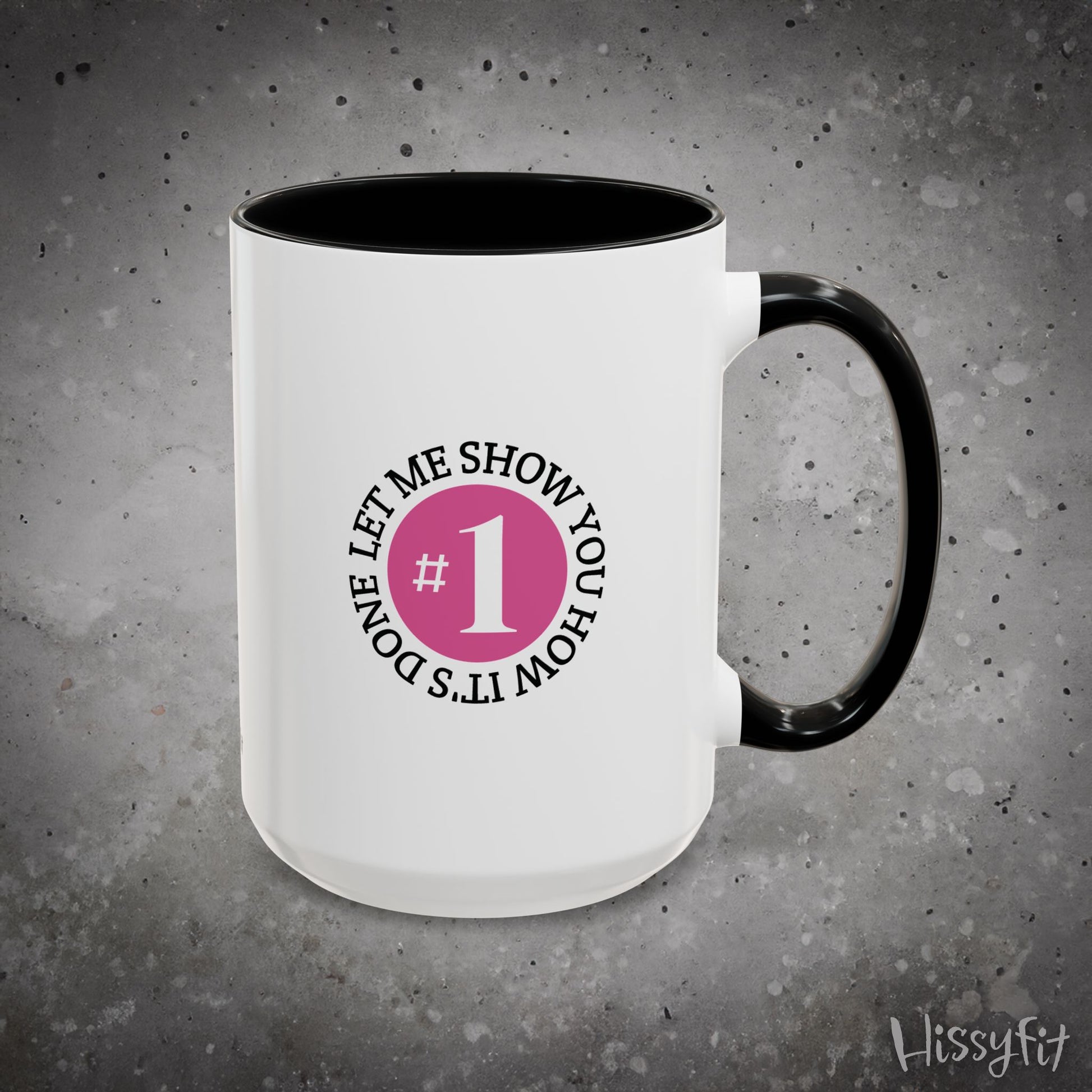 White mug with black interior and handle featuring a graphic with text 'Let me show you how it's done, #1' on a gray background.