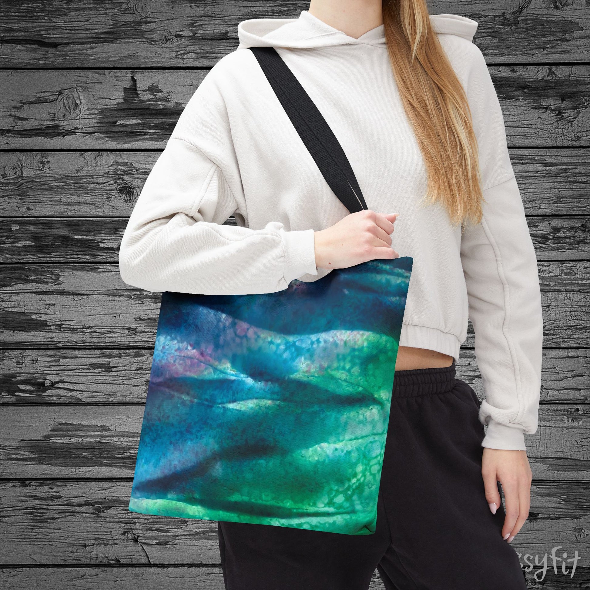 Person holding a tote bag with a blue and green abstract design against a wooden background