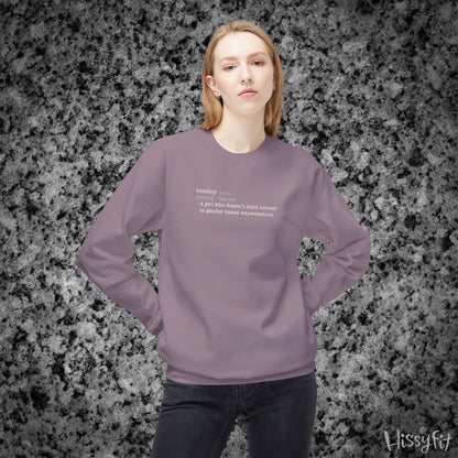 Person wearing a light purple sweatshirt with text definition of "Tomboy" on a gray and black speckled background