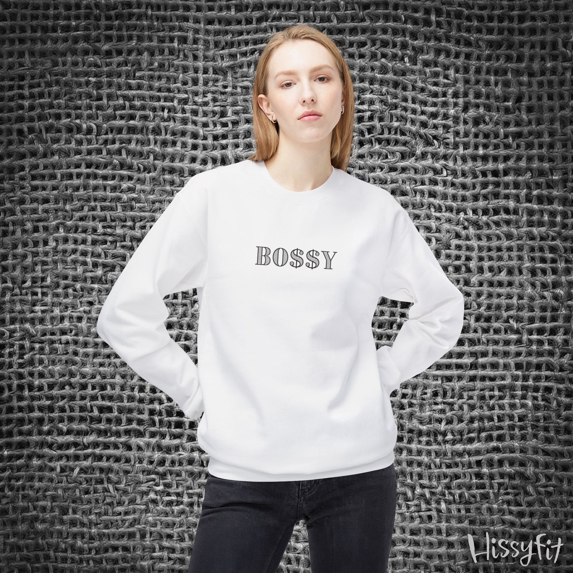 Person wearing a white sweatshirt with 'BOSSY' text against a textured gray wall.