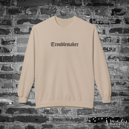 Beige sweatshirt with 'Troublemaker' text on a brick wall background