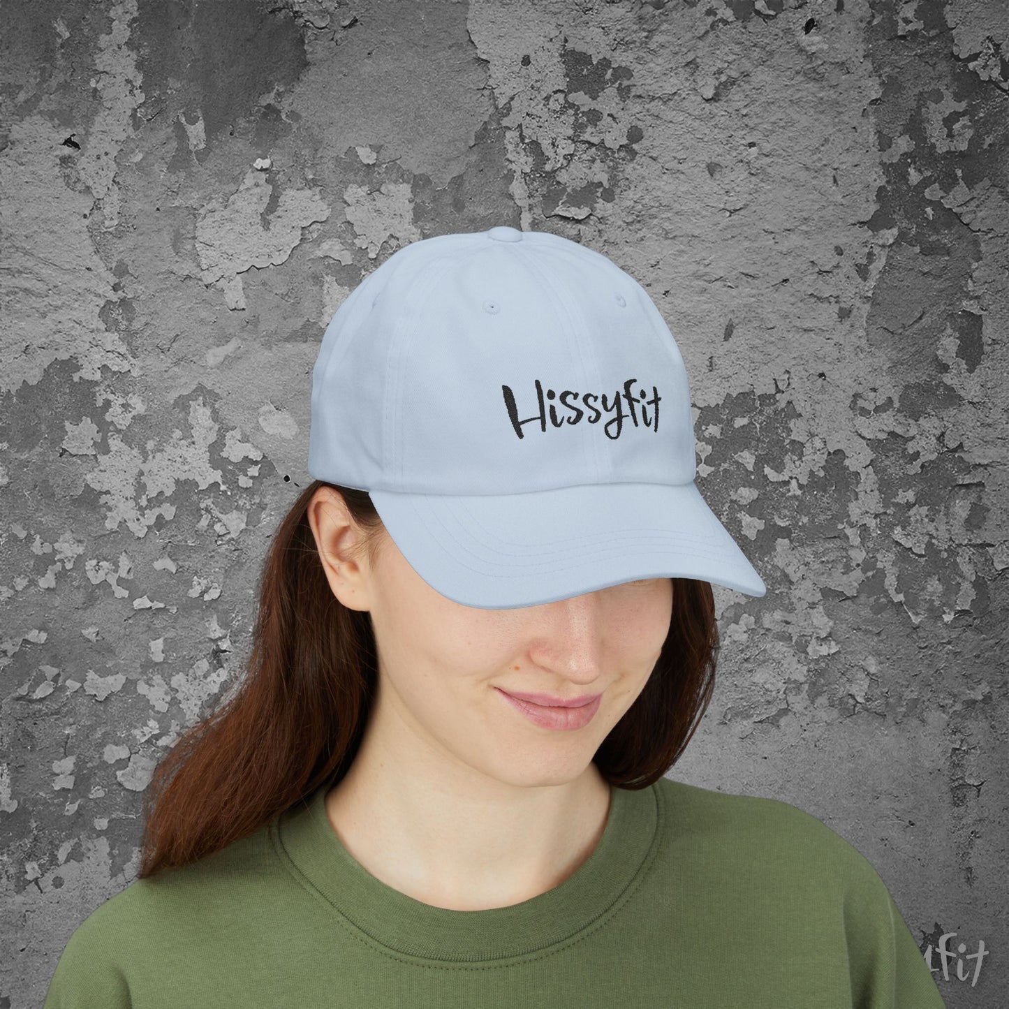 Person wearing a light blue cap with 'Hissyfit' text against a textured gray wall.