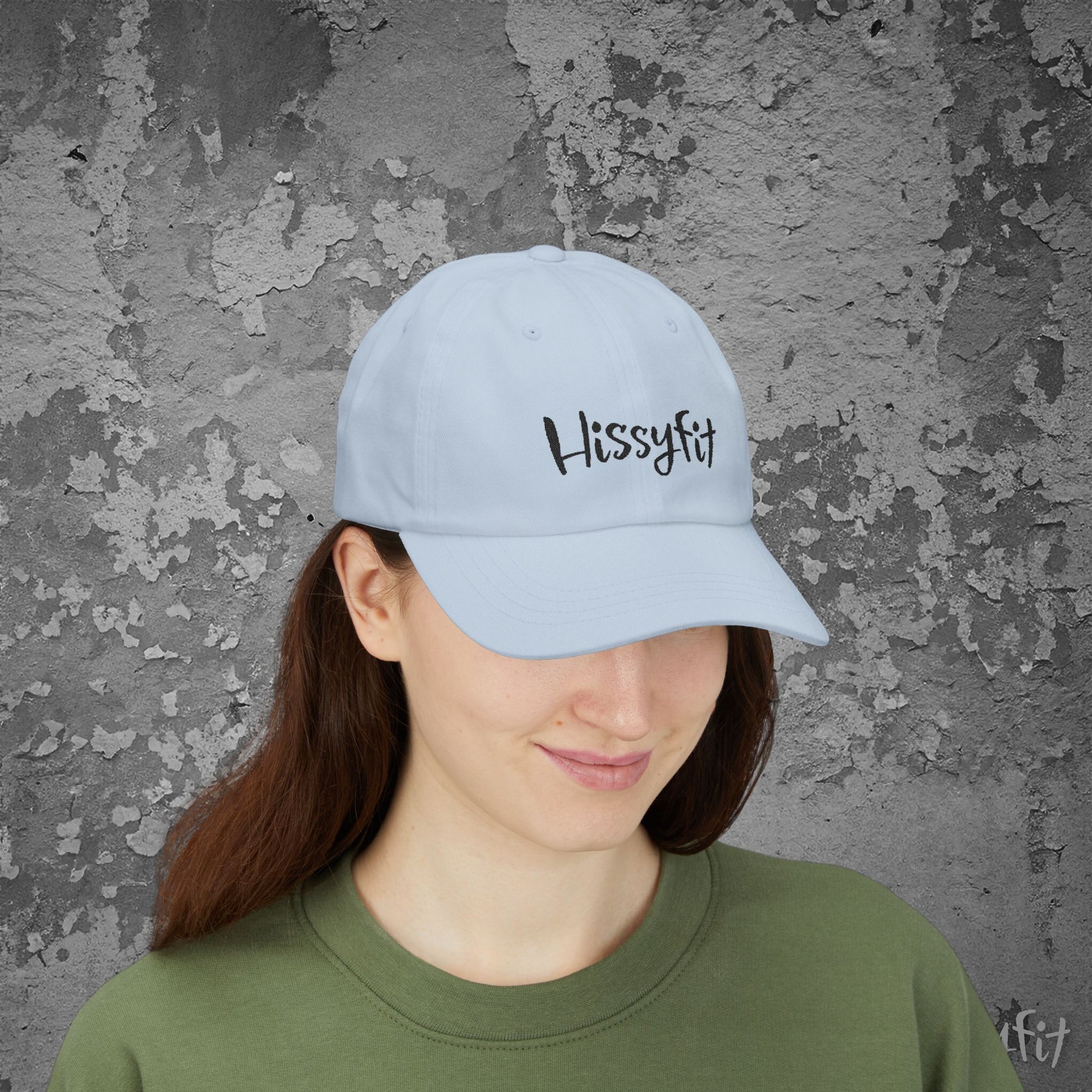 Person wearing a light blue cap with 'Hissyfit' text against a textured gray wall.