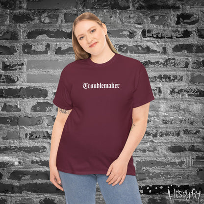 Person wearing a maroon t-shirt with 'Troublemaker' text against a textured wall.