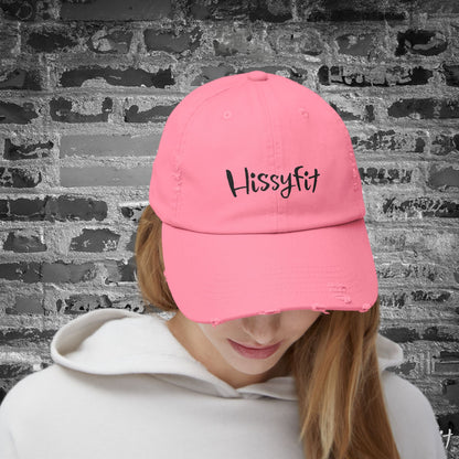 Person wearing a pink cap with 'Hissyfit' text against a textured wall background