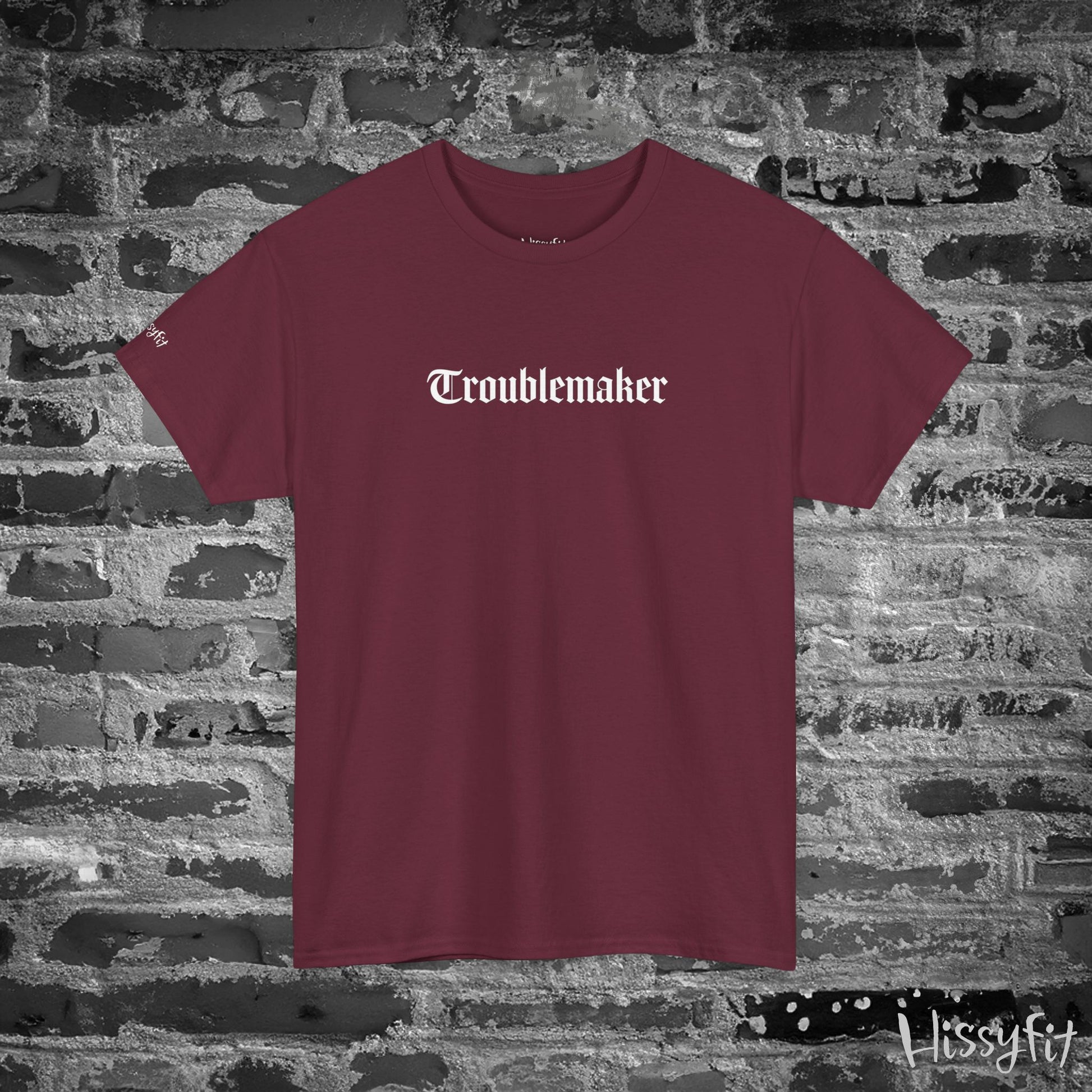 Maroon t-shirt with 'Troublemaker' text on a stone wall background