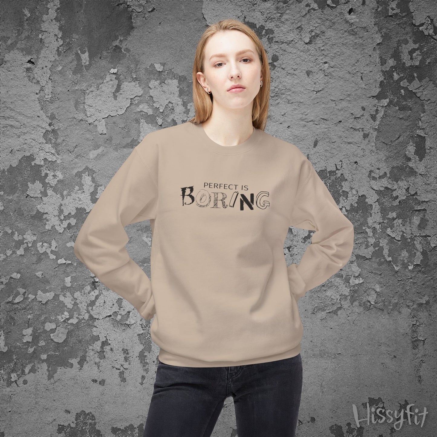 Person wearing a beige sweatshirt with 'PERFECT IS BORING' text against a textured gray background