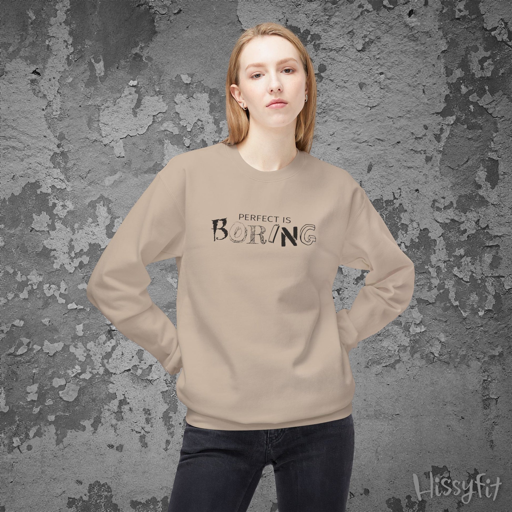 Person wearing a beige sweatshirt with 'PERFECT IS BORING' text against a textured gray background