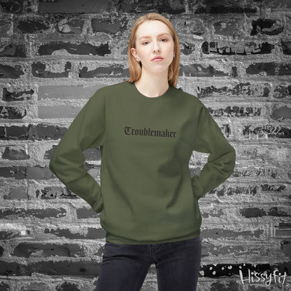 Person wearing a green sweatshirt with 'Troublemaker' text against a textured brick wall.