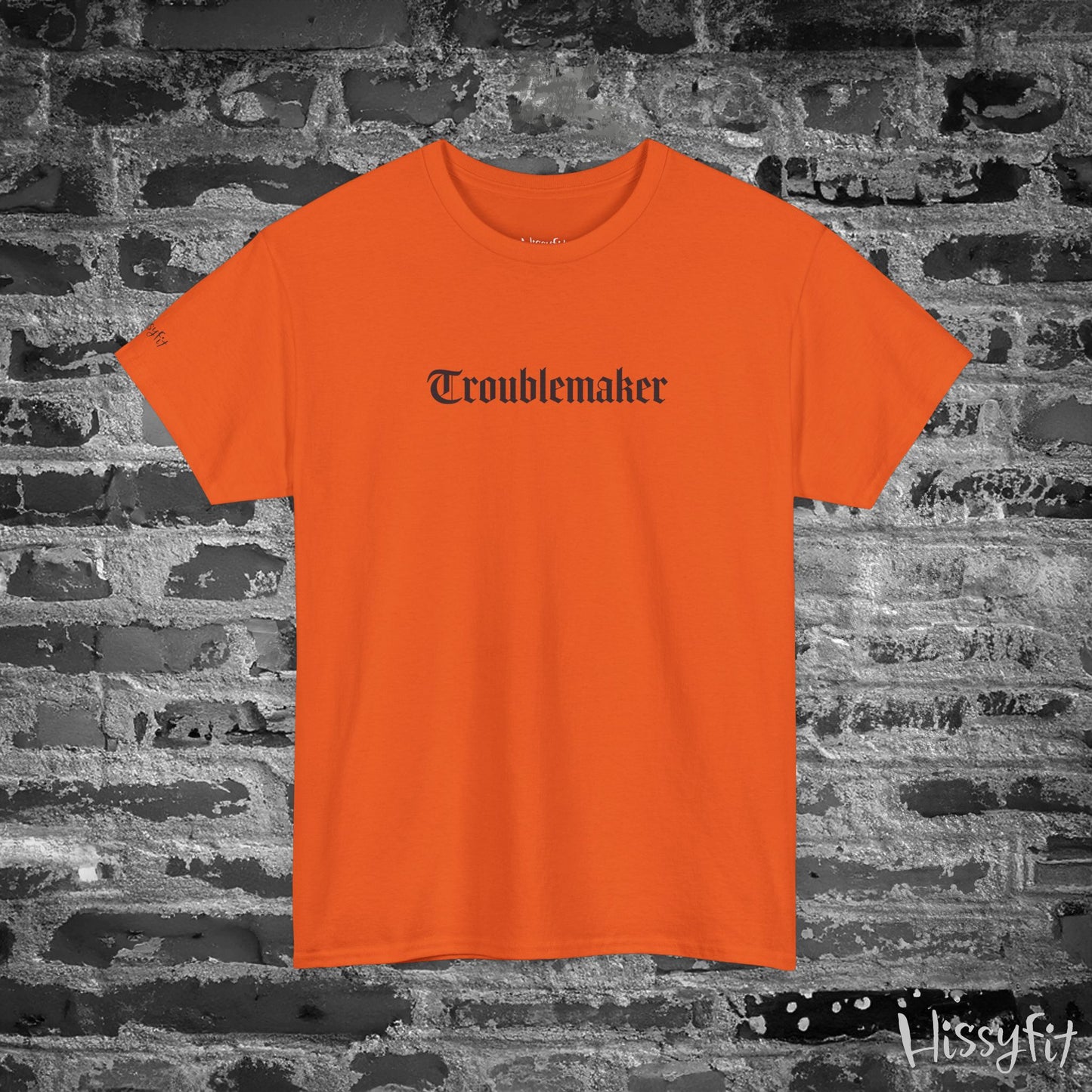 Orange t-shirt with 'Troublemaker' text on a brick wall background