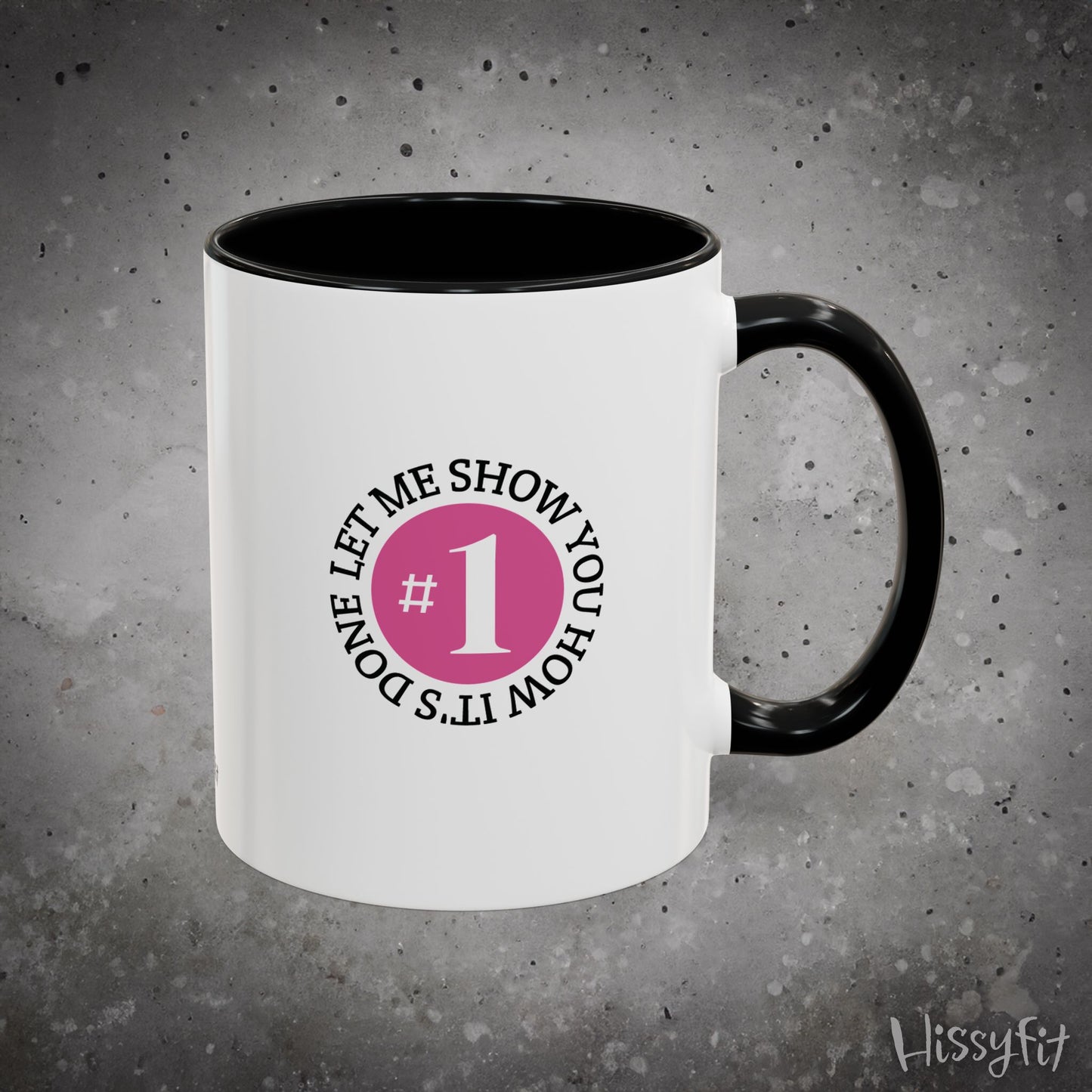 White mug with black interior and handle, featuring a graphic with text 'Let me show you how it's done, #1' on a gray background.