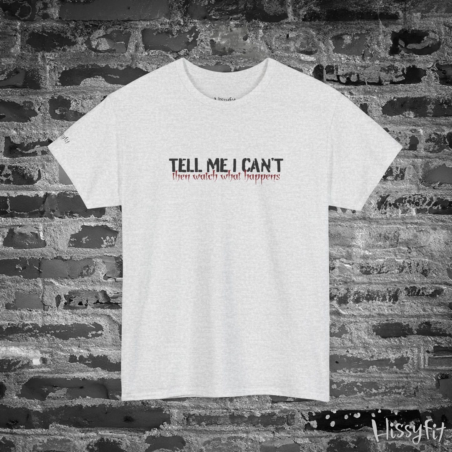 White t-shirt with text 'Tell me I can't then watch what happens' on a brick wall background