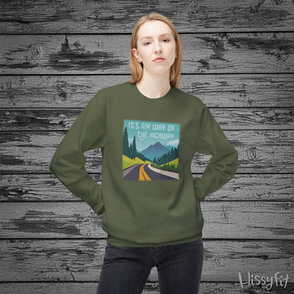 Person wearing a green sweatshirt with a graphic design of a road and mountains and "It's my way or the highway" text on a wooden background