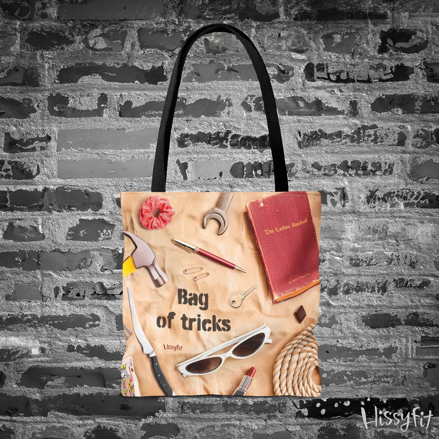 Tote bag with various items and text 'Bag of tricks' against a brick wall background