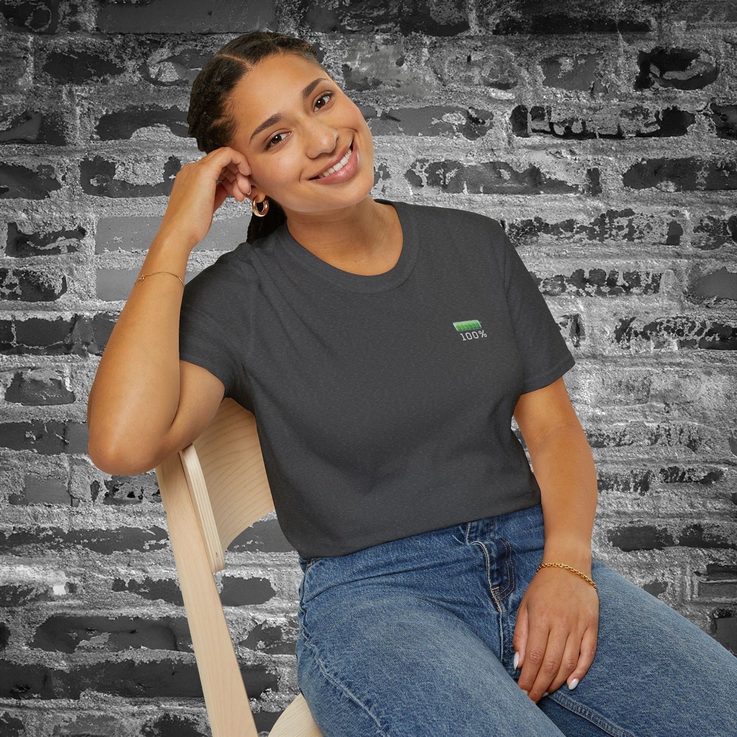 Woman wearing a dark gray t-shirt with a green battery symbol displaying '100 percent charged' on a brick wall background
