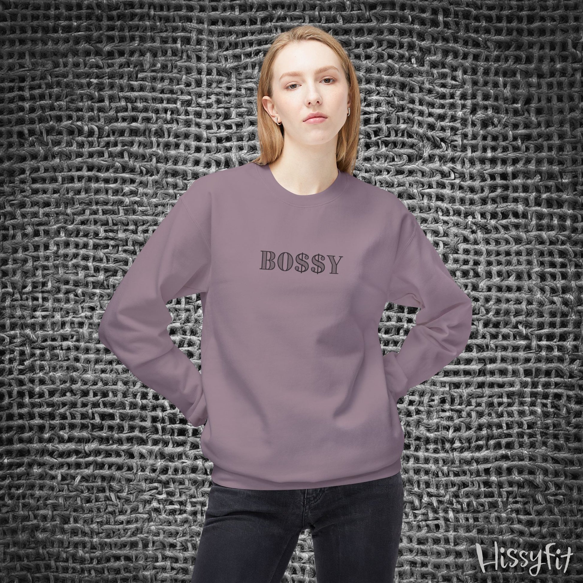 Person wearing a purple sweatshirt with 'BOSSY' text against a textured gray background