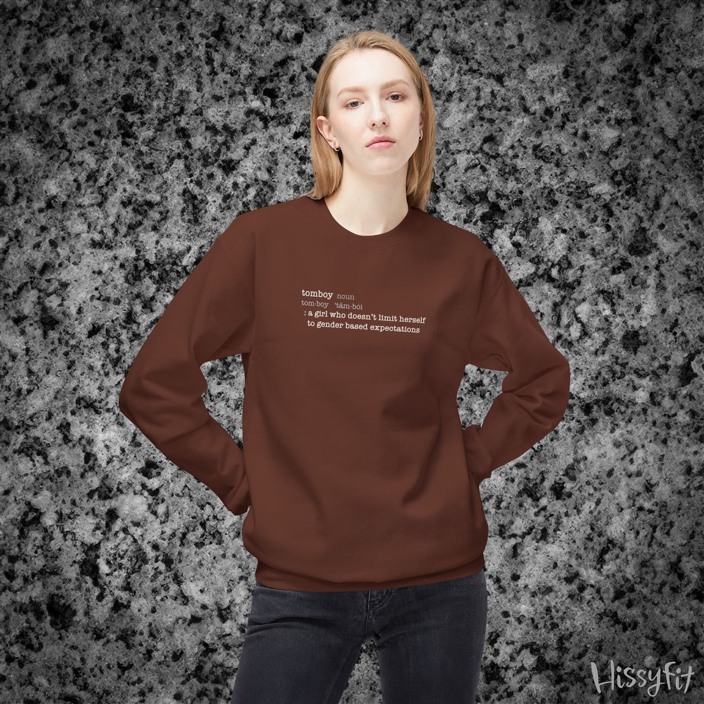 Person wearing a brown sweatshirt with text definition of "Tomboy" on a gray and black speckled background