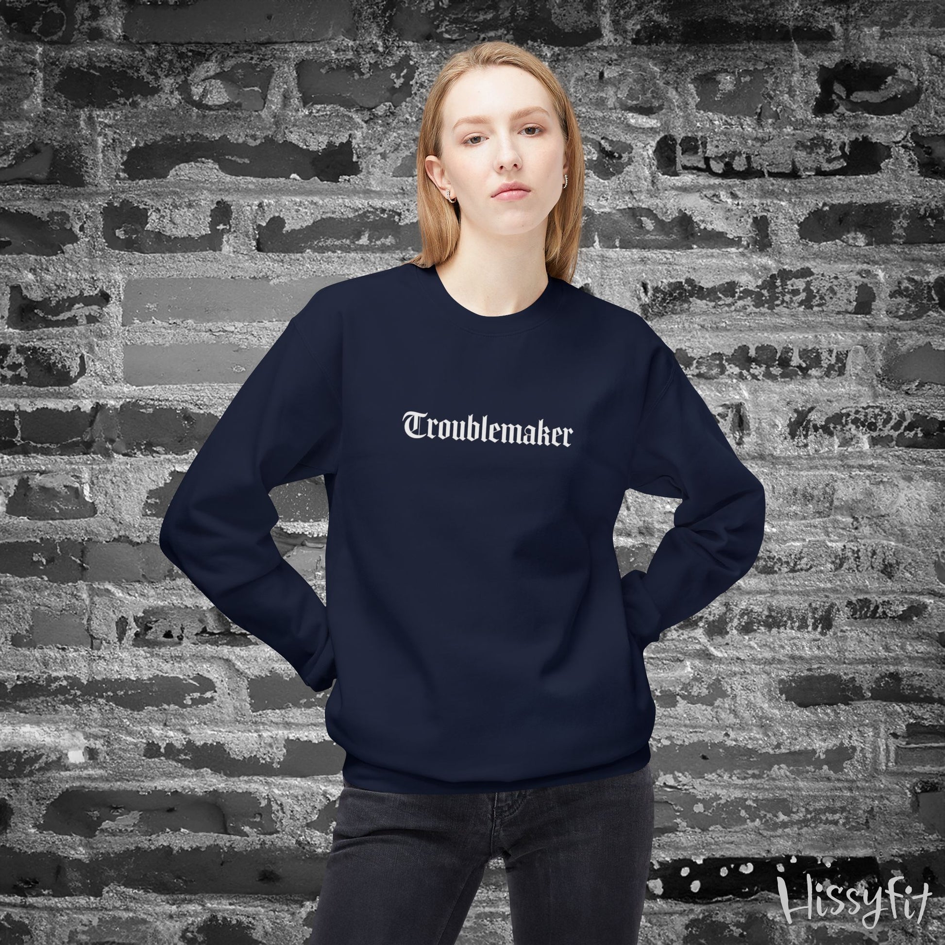 Person wearing a navy blue sweatshirt with 'Troublemaker' text against a textured brick wall.