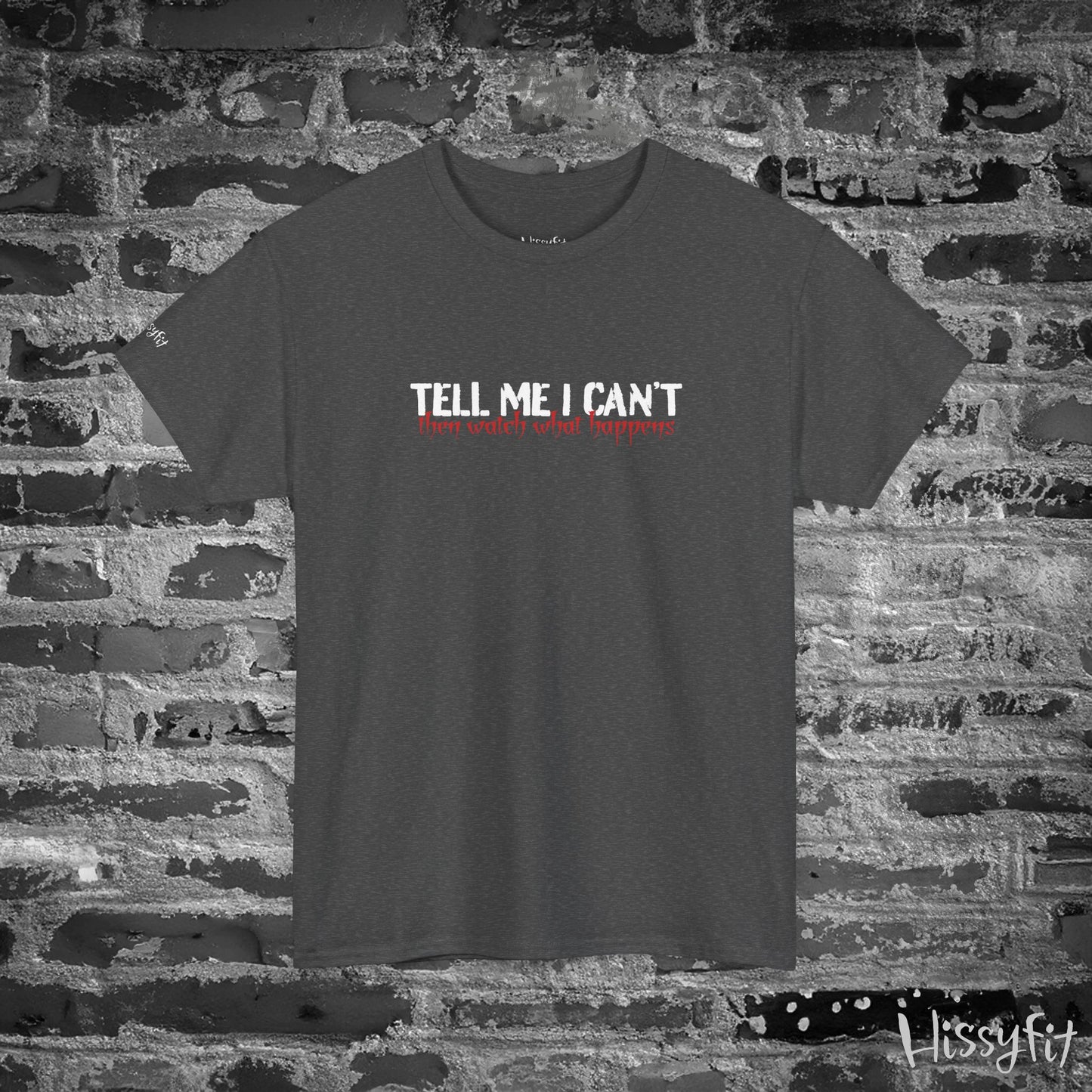Black t-shirt with 'Tell Me I Can't then watch what happens' text on a brick wall background