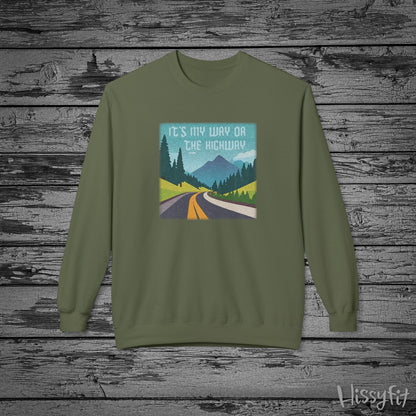 Green sweatshirt with a graphic design of a road and mountains and "It's my way or the highway" text on a wooden background
