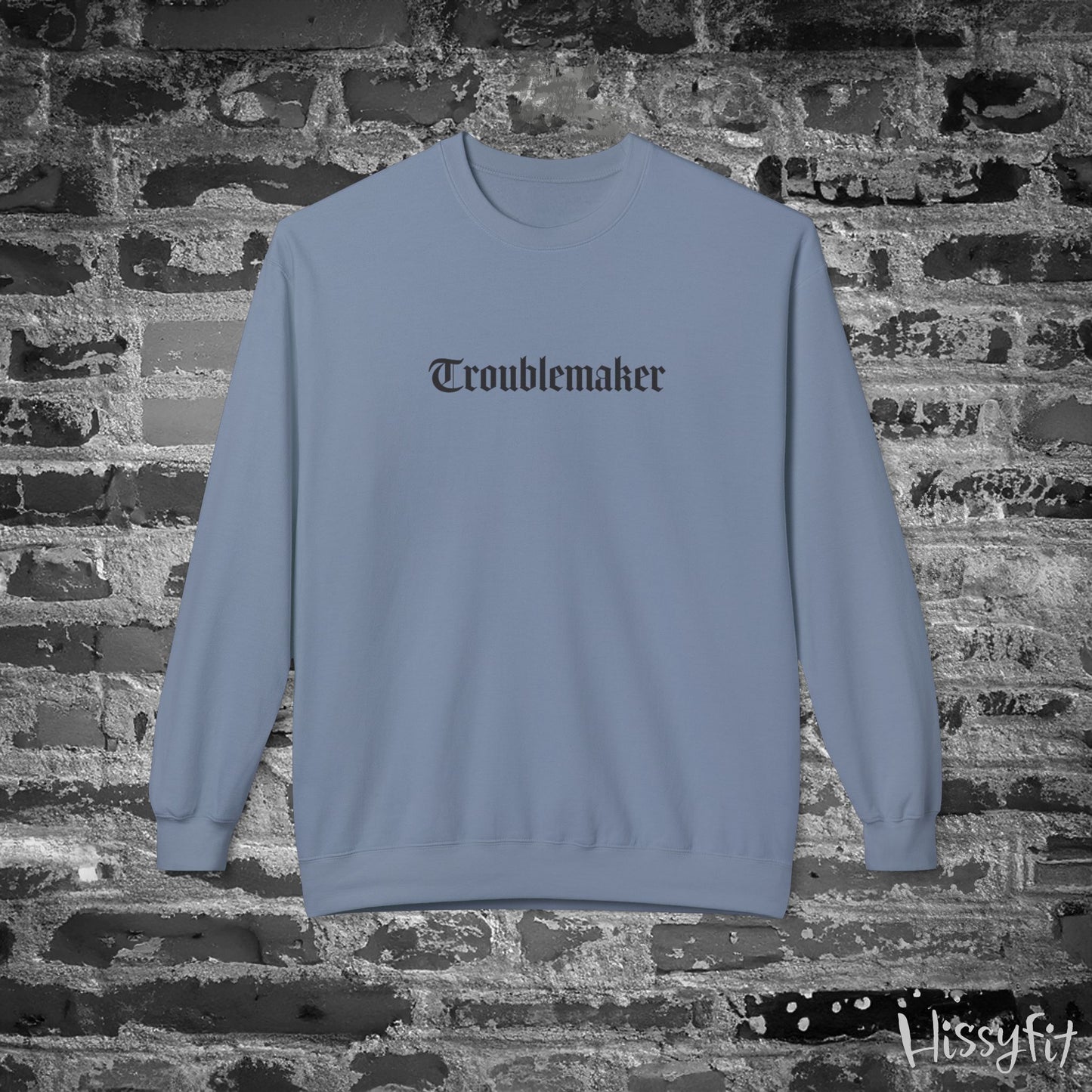 Blue sweatshirt with 'Troublemaker' text on a brick wall background