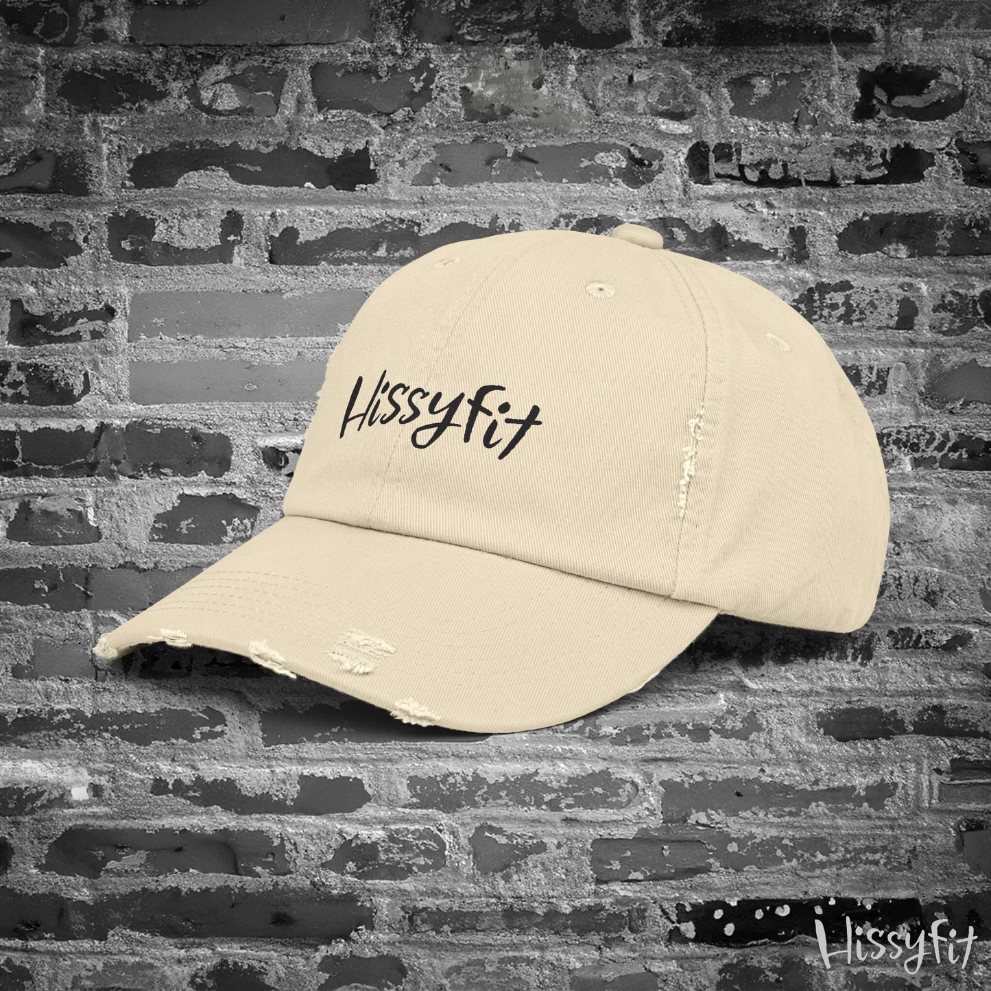 Beige cap with 'Hissyfit' logo on a textured brick wall background
