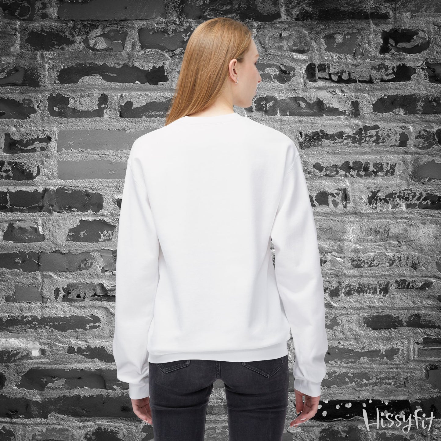 Person wearing a white sweatshirt standing against a textured brick wall.