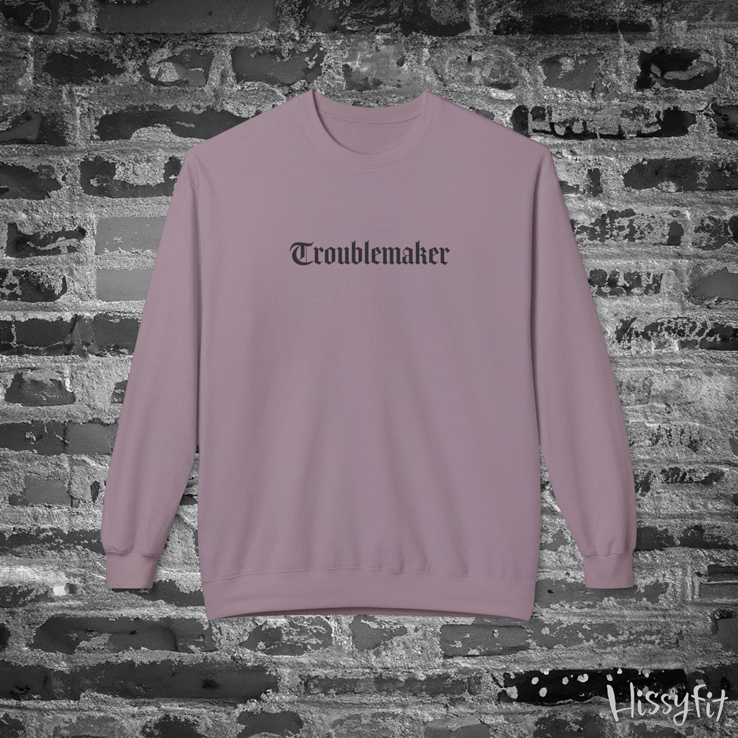 Mauve sweatshirt with 'Troublemaker' text on a brick wall background