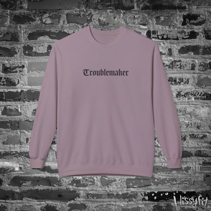 Mauve sweatshirt with 'Troublemaker' text on a brick wall background
