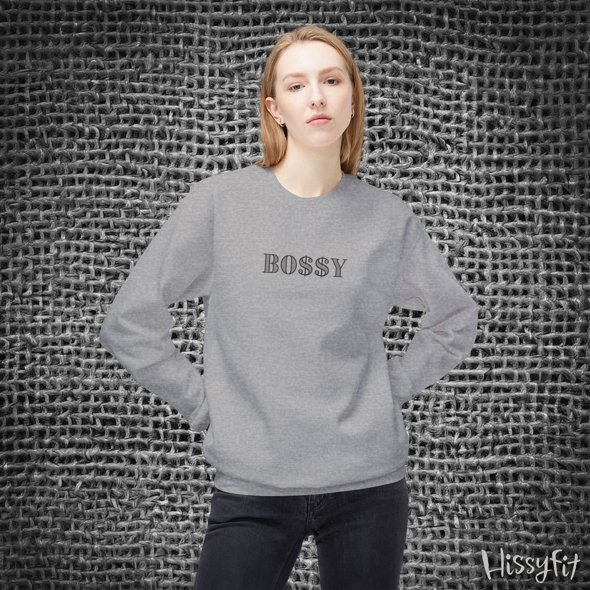 Person wearing a gray sweatshirt with 'BOSSY' text against a textured wall.