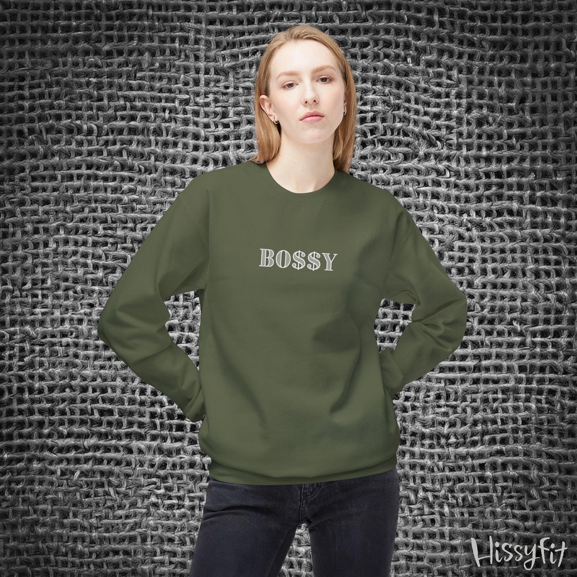Person wearing a green sweatshirt with 'BOSSY' text against a textured gray background