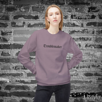 Person wearing a purple sweatshirt with 'Troublemaker' text against a textured wall.