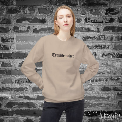 Person wearing a beige sweatshirt with 'Troublemaker' text against a textured brick wall.