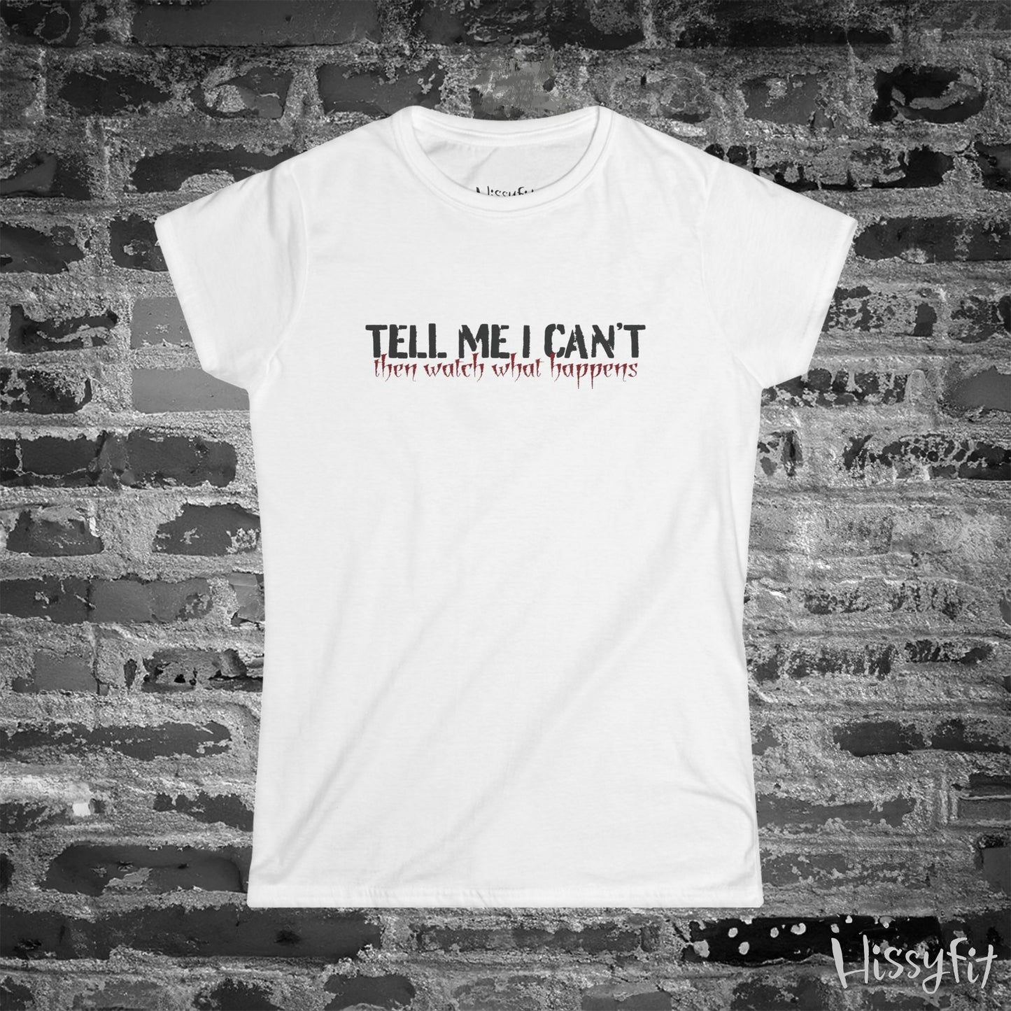 White t-shirt with text 'Tell me I can't then watch what happens' on a brick wall background