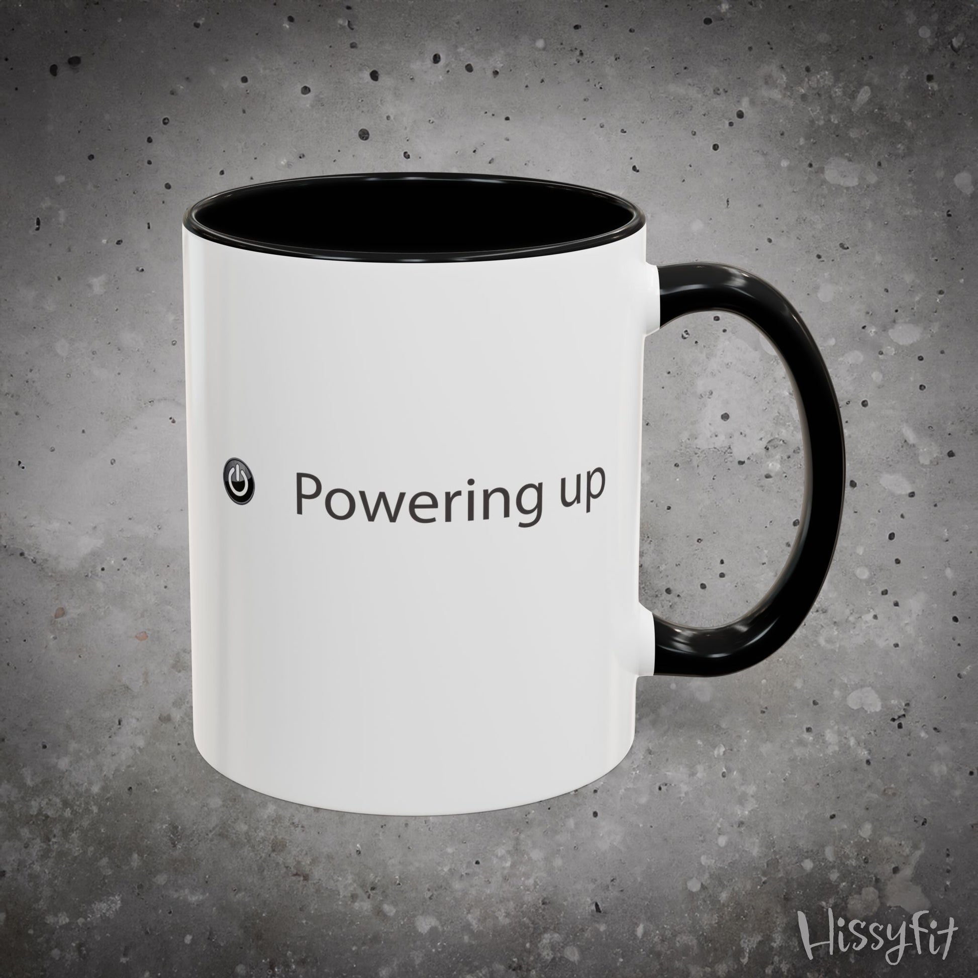 White mug with black interior and handle on a gray background, featuring the text 'Powering up' and a logo.