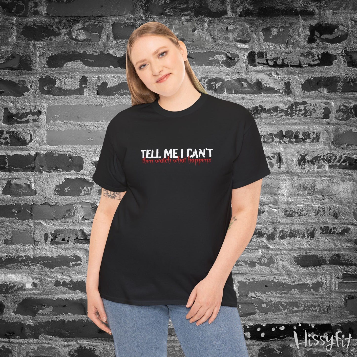 Person wearing a black t-shirt with text 'Tell me I can't then watch what happens' in front of a textured wall