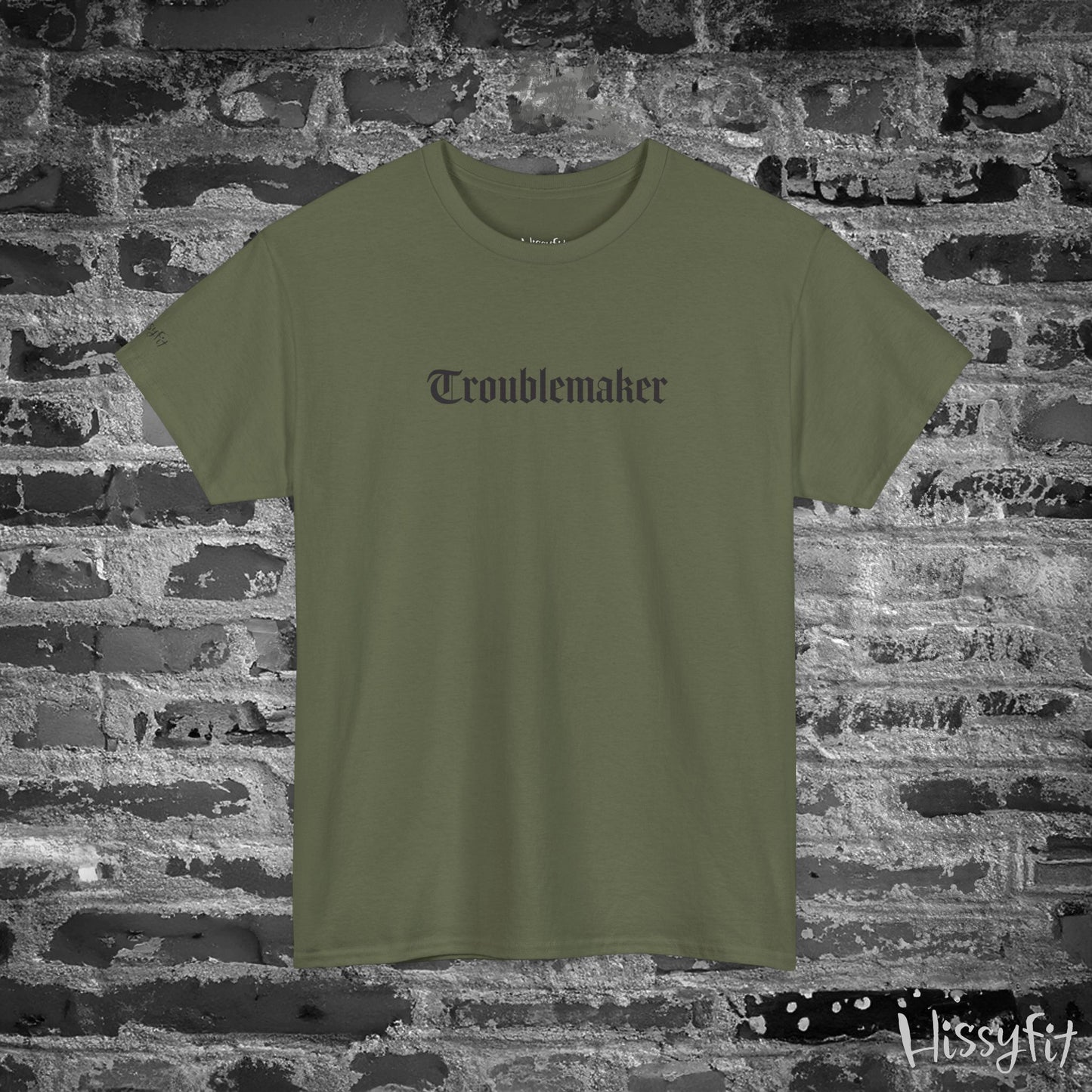 Green t-shirt with 'Troublemaker' text on a brick wall background