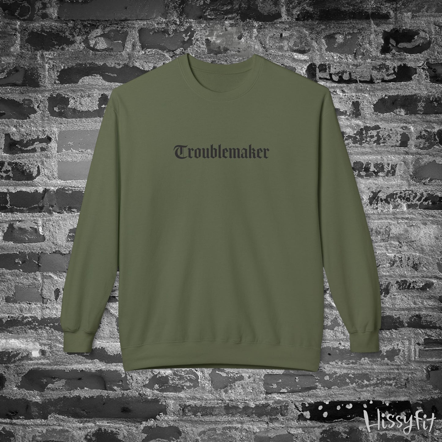 Green sweatshirt with 'Troublemaker' text on a brick wall background