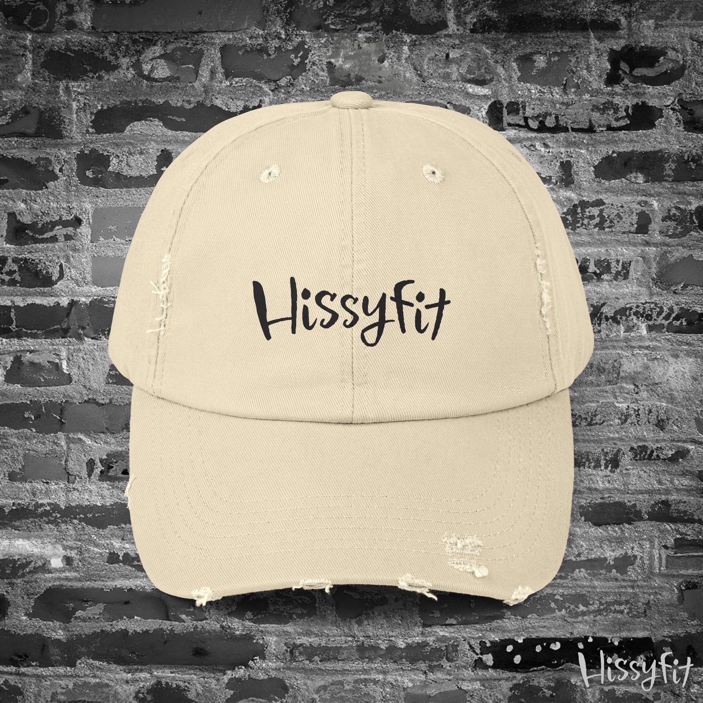 Beige cap with 'Hissyfit' text on a brick wall background