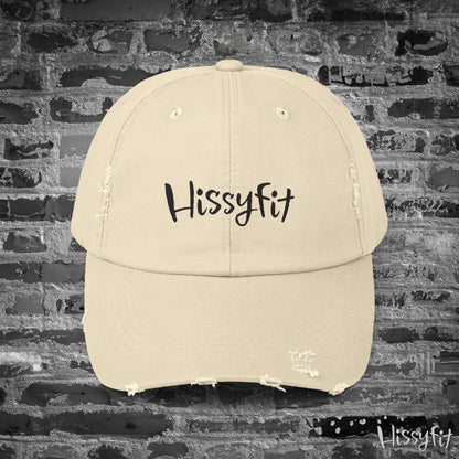 Beige cap with 'Hissyfit' text on a brick wall background
