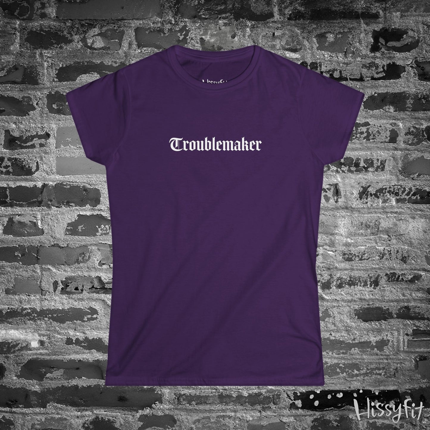 Purple t-shirt with 'Troublemaker' text on a brick wall background