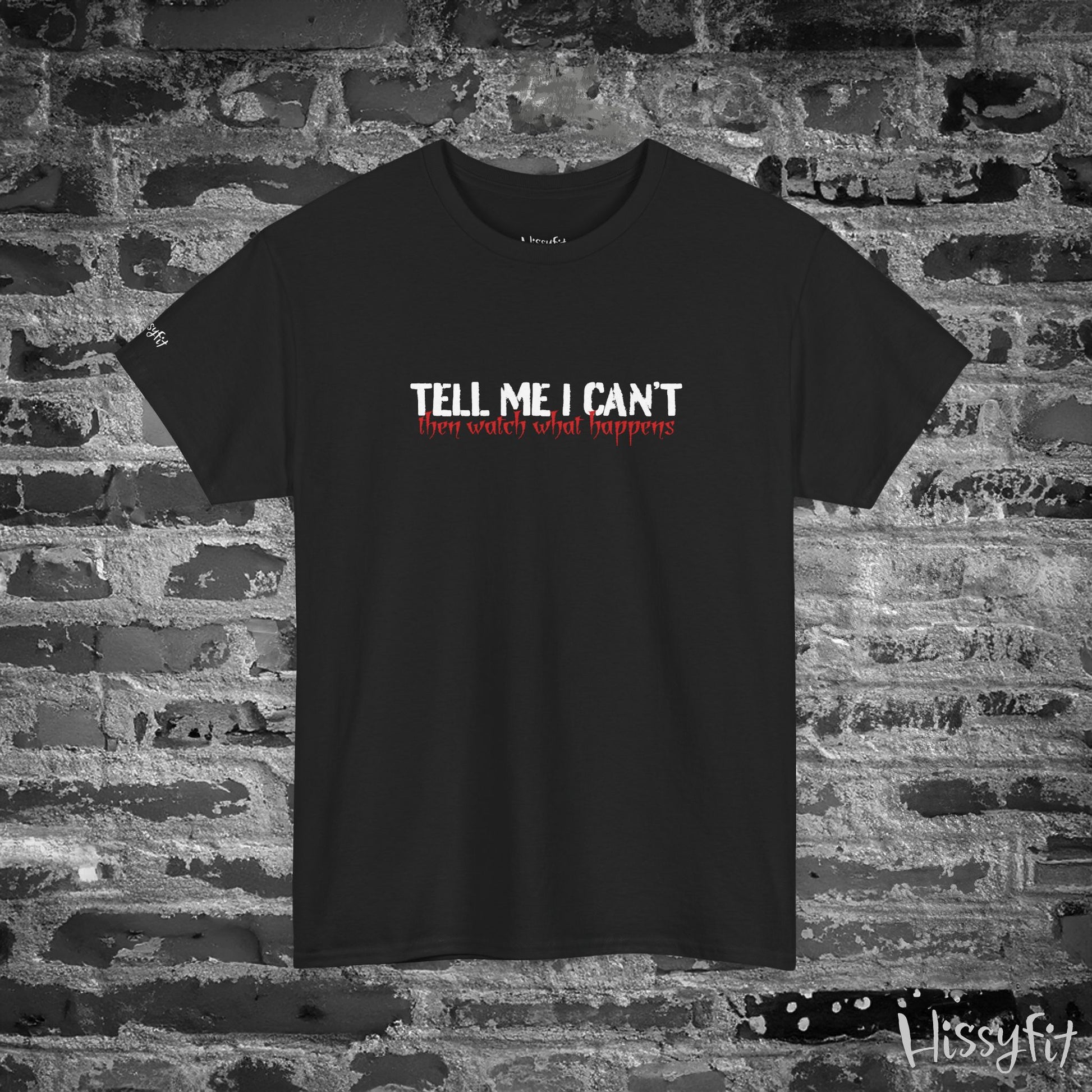 Black t-shirt with 'Tell me I can't then watch what happens' text on a brick wall background