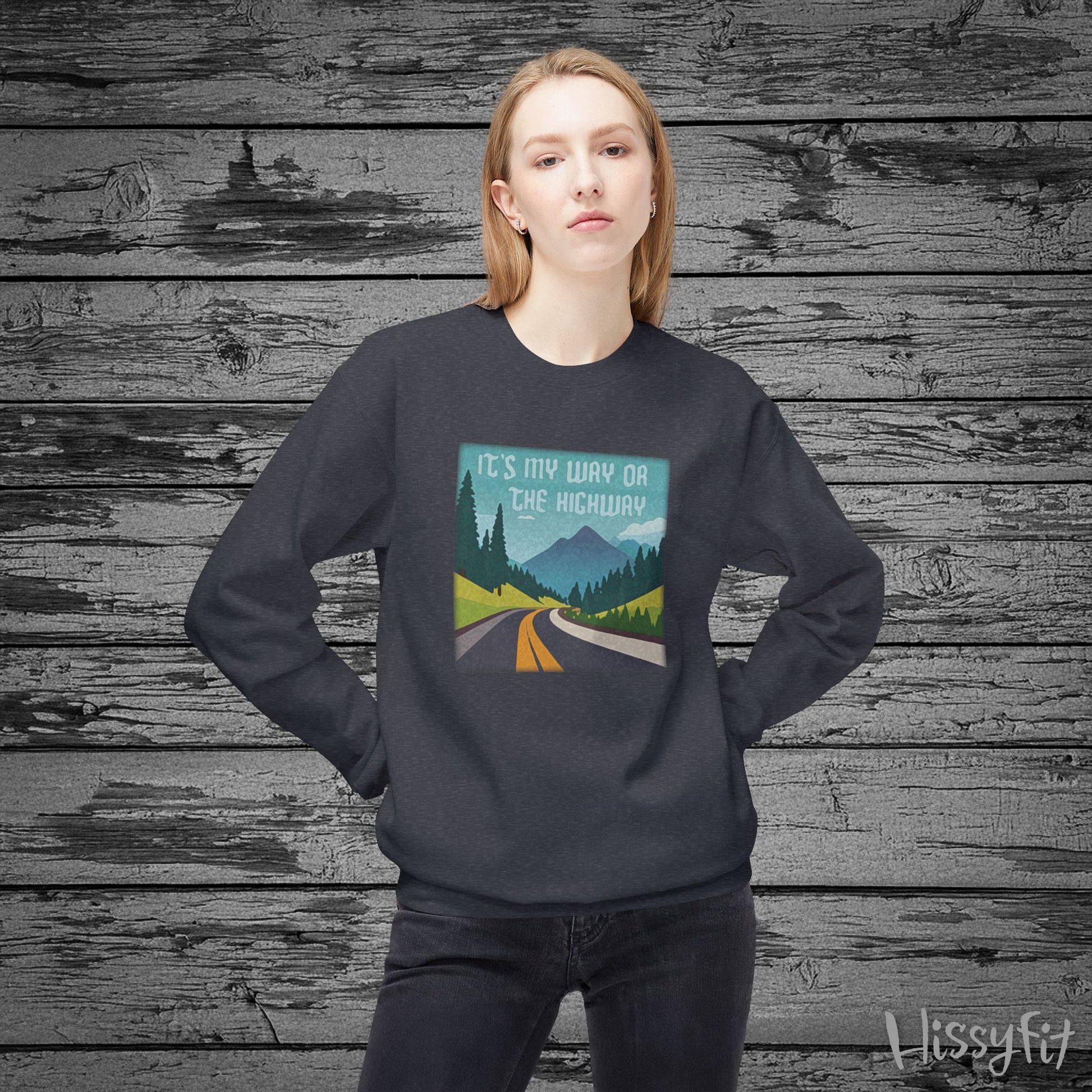 Person wearing a dark gray sweatshirt with a graphic design of a road and mountains and "It's my way or the highway" text on a wooden background